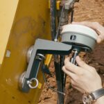 Hands fitting the GNSS receiver onto its magnetic holder on an excavator stick